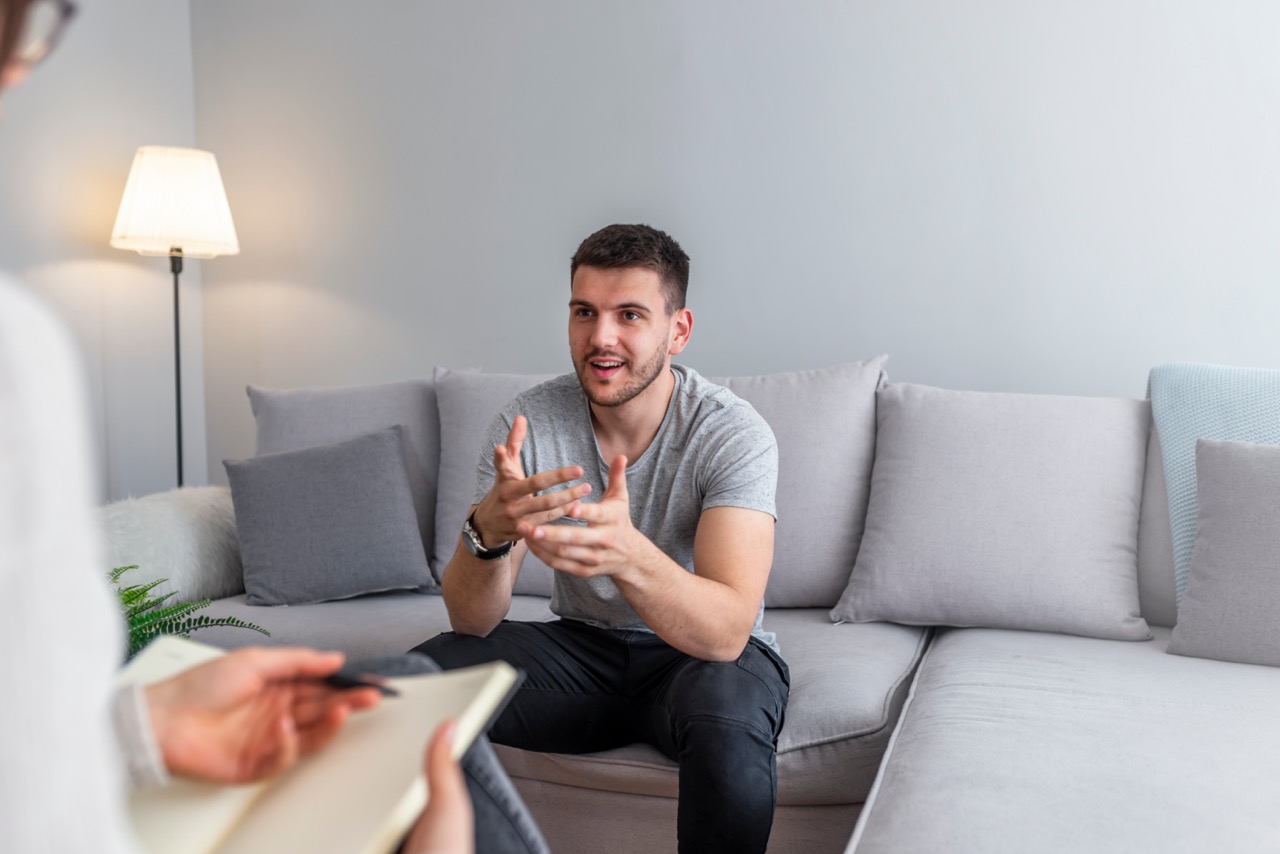 Psychologist talking with happy man in the office. Image of young man during psychological therapy. Female psychologist consulting man during psychological therapy session